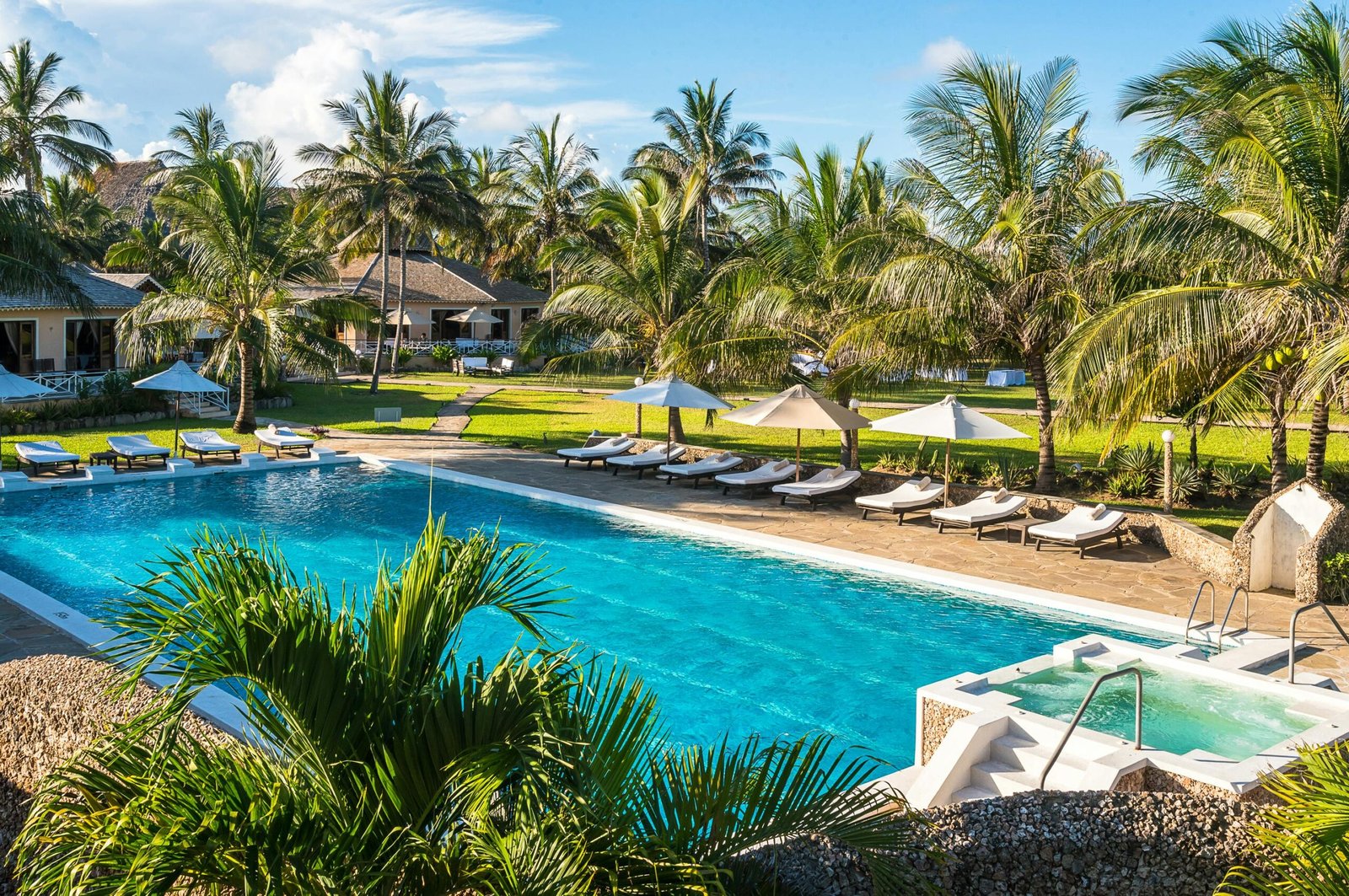 Enjoy a relaxing day at a luxurious resort pool surrounded by palm trees in Malindi, Kenya.